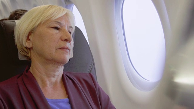 坐飞机的老妇人。因时差而疲惫的女性在乱流中靠近窗户放松视频素材