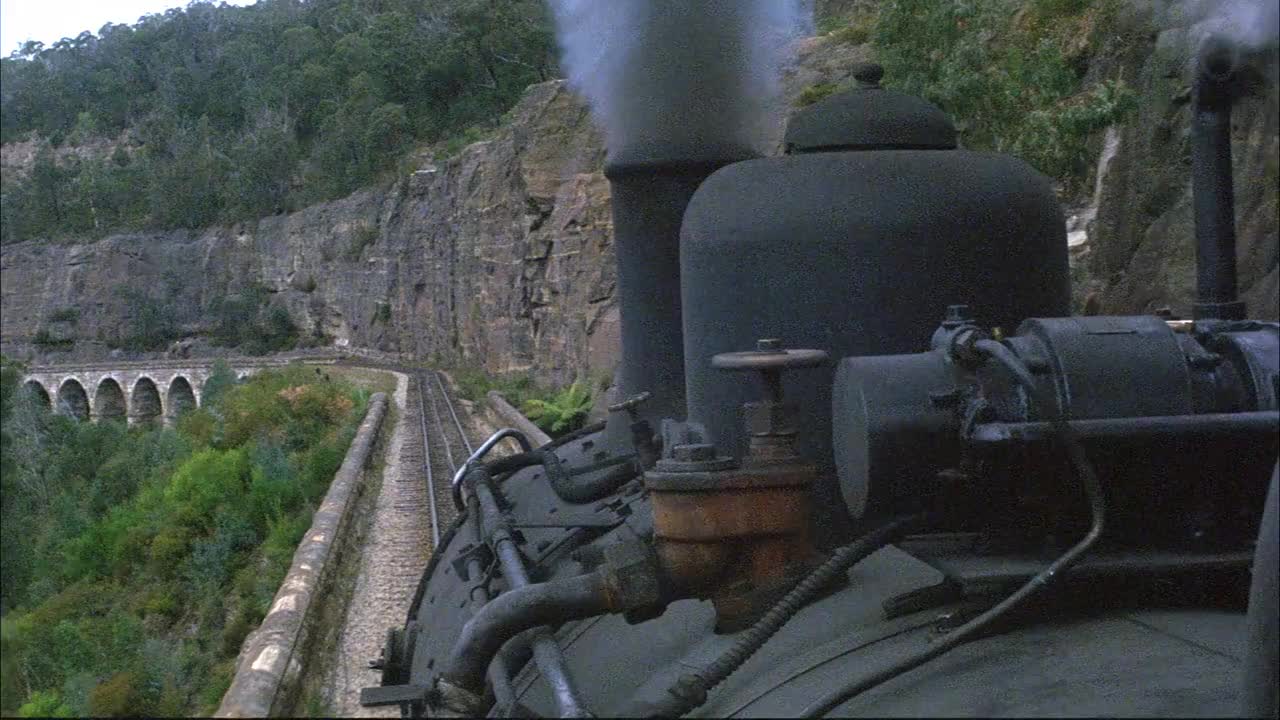中等角度的pov安装在黑色蒸汽机列车。看火车沿着轨道行驶。看到蒸汽从顶部的通风口滚滚而出。右侧见灰色岩壁。视频素材
