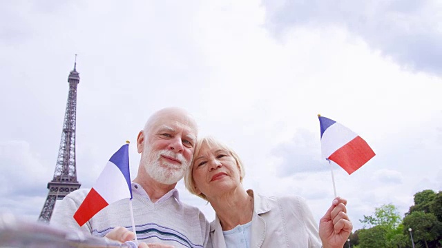 一对老年夫妇在埃菲尔铁塔附近举着法国国旗自拍。微笑的游客在欧洲旅行视频素材