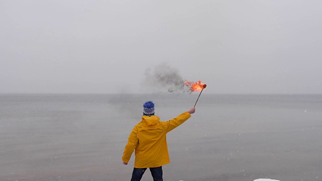 后视图的人与火火炬在黄色大衣的背景上冻结的海。前景下雪视频素材