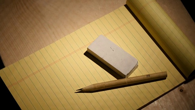 用橡皮擦翻黄色的记事本和铅笔视频素材