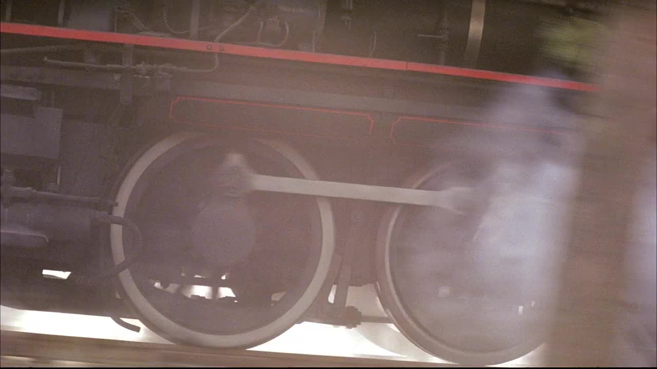 森林中黑色蒸汽火车的跟踪镜头。看蒸汽从火车上升起。参见车厢和发动机的轮子。看到山丘挡住了火车的前进方向，只有发动机的顶部除外。看到货车车厢和车轮沿着铁轨滚动。在背景中看到森林。视频素材