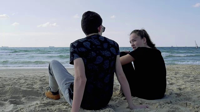 青少年，女孩和男孩坐在海滩上聊天。视频下载