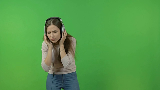 漂亮的长发女孩，戴着耳机听音乐。在绿色屏幕上。她又跳舞又唱歌。视频下载