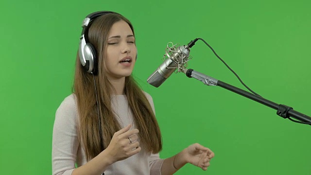 一个小女孩正对着录音室的麦克风唱歌。特写镜头。在绿色的背景上。视频素材