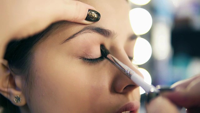 专业化妆师用化妆刷涂抹眼影的手的特写视图。Pro visagiste将浅棕色的眼影涂在模特的眼睑上。Slowmotion拍摄视频素材