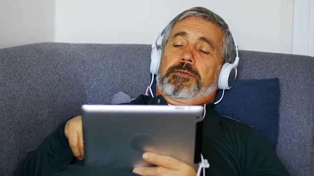 男人躺在沙发上用数码平板电脑听音乐视频素材