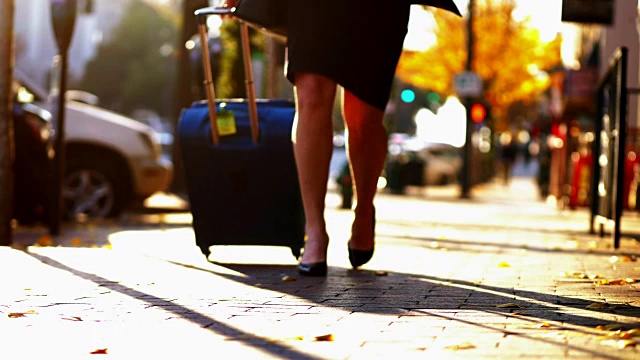 在城市的人行道上拉着行李箱的女商人。视频素材