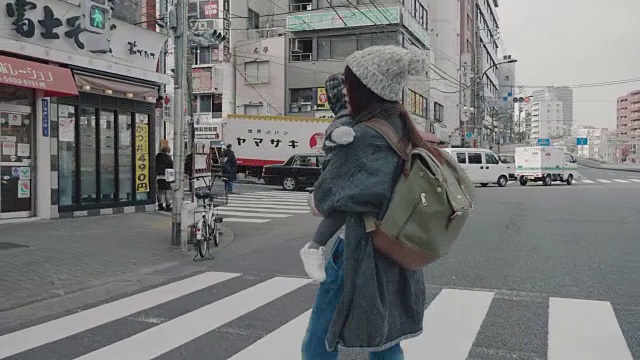 亚洲母亲抱着婴儿(12个月)走在街上。视频下载