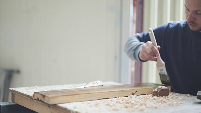 一个年轻人正在用棕色油漆油漆木板。视频下载