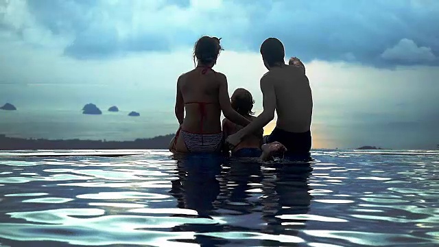 妈妈爸爸和他们的儿子拥抱坐在游泳池部分与无限的海景山顶在慢镜头。1920 x1080视频下载