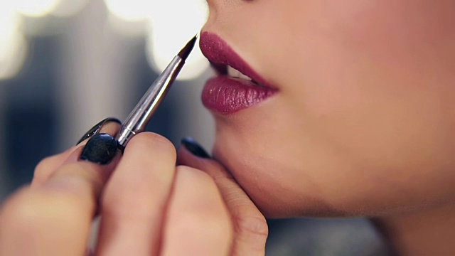 不可辨认的专业化妆师，用特殊的刷子在模特的嘴唇上涂口红视频素材