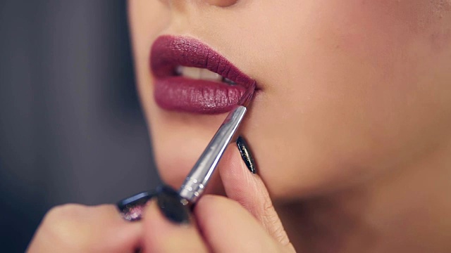 一个专业的化妆师的手使用特殊的刷子应用口红或唇彩模特的嘴唇在美容时尚行业工作的特写视图。Slowmotion拍摄视频购买