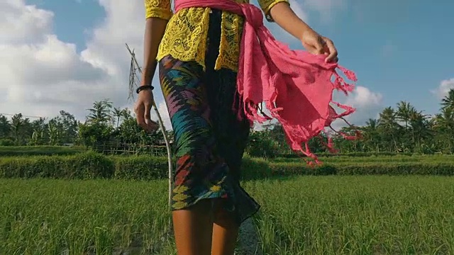 美丽的年轻女子走在稻田的中间，穿着巴厘岛的服装，周围是棕榈树加上过渡到黑色视频素材