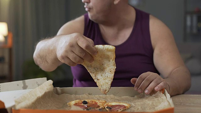 超重男性晚上吃披萨很快，对不健康的食物上瘾视频素材