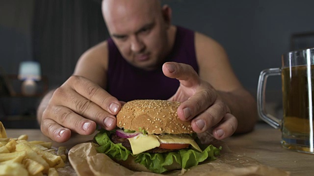 暴饮暴食，胖男人做大汉堡，美食家欣赏他的饭菜，特写视频素材