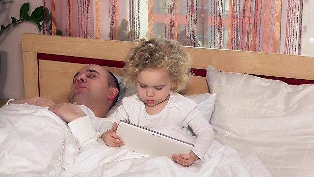 秃顶的爸爸睡着了，而女儿在床上玩平板电脑视频下载