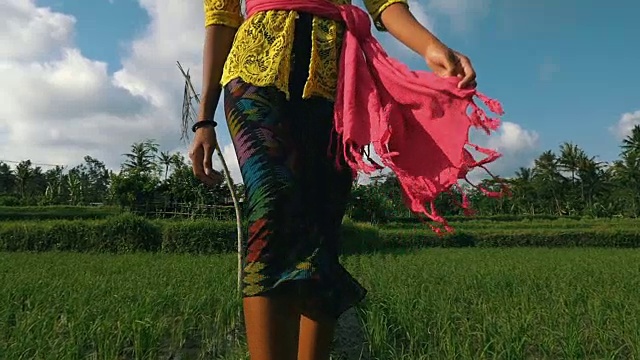 年轻美丽的女人穿着巴厘服装微笑着走在棕榈树环绕的稻田中间视频素材
