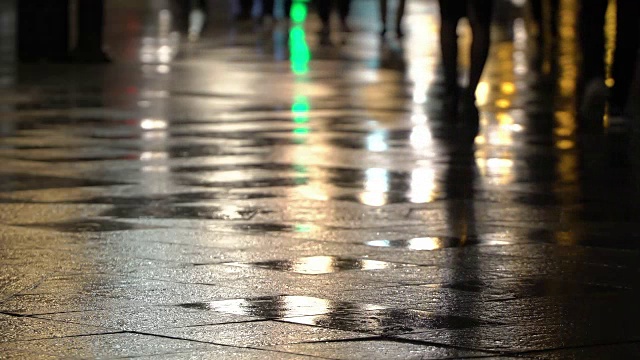 在潮湿的人行道上，街灯映出了辨认不出的人的剪影。长长的影子。雨夜的城市街道上有路灯，沥青路从雨中闪闪发光。不认识的行人，年轻人。夜晚的城市下雨。购物的概念视频素材