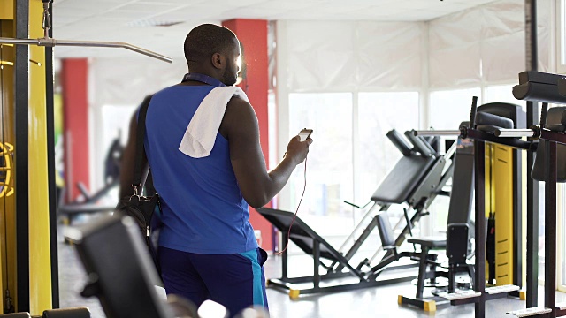 英俊的运动员在健身房听音乐，在智能手机上选歌视频素材