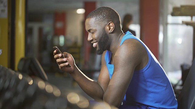 一名年轻人面带微笑在智能手机上打字，在锻炼中休息视频素材