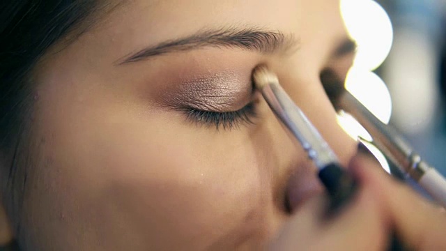 专业化妆师使用两个化妆刷涂抹眼影。Pro visagiste将浅棕色的眼影涂在模特的眼睑上。Slowmotion拍摄视频素材