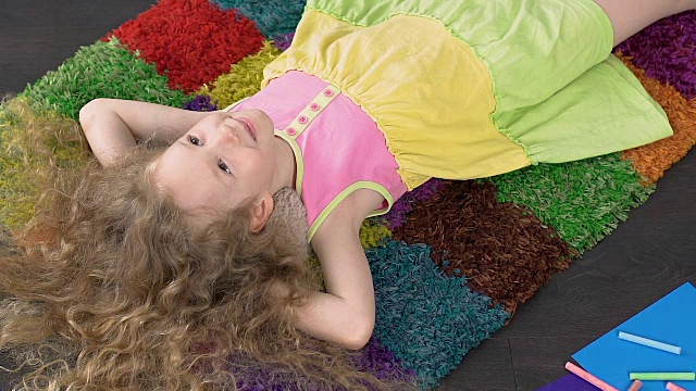 美丽的小女孩躺在家里五颜六色的地毯上笑着，幸福极了视频下载