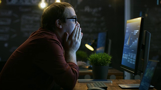 紧张的金融家沮丧地用拳头打桌子，用手捂着脸。他正在用一个显示在屏幕上的统计数据的个人电脑工作。视频素材