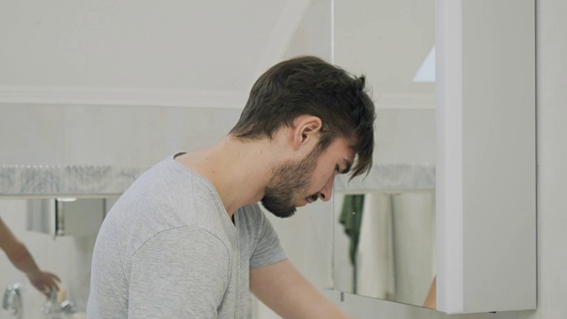 一个昏昏欲睡的年轻人在镜子前用牙刷刷牙视频素材