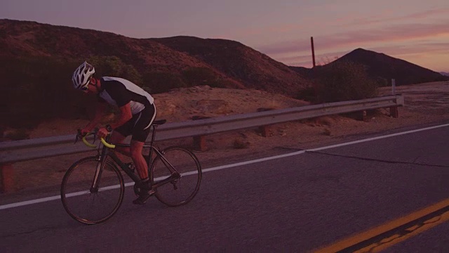 慢动作健身男子在公路自行车上锻炼在日落时分骑上山视频素材