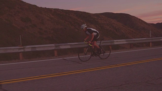 慢动作健身男子在公路自行车上锻炼在日落时分骑上山视频素材