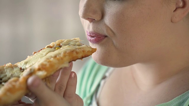 胖乎乎的女人在吃前对着热披萨片吹气，快餐和肥胖视频素材
