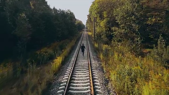 在秋天森林铁路上奔跑的人。无人机的后视图。运动员在道路上清晰的视野地平线。电影的拍摄视频素材