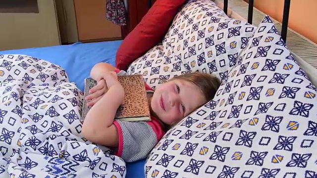 小女孩在床上。女孩想拿着父亲的日记入睡。小女孩的床上放着一本旧书。家庭的概念视频下载