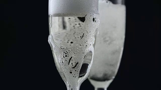 香槟从酒瓶中倒入黑色背景的两个玻璃杯中。近距离视频素材