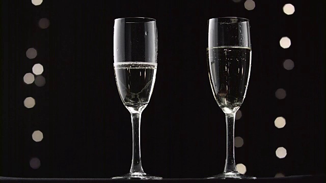 香槟被倒入两个透明的玻璃杯中。散景闪烁的黑色背景视频素材