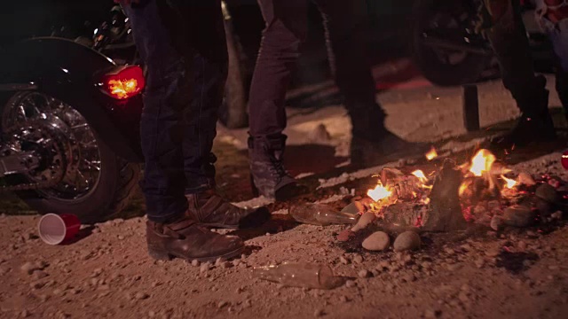 在聚会期间，摩托车手围绕篝火的腿的特写视频素材