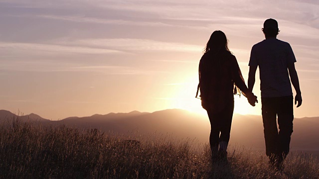 一对夫妇在山顶上走向夕阳的慢动作，他们转身亲吻视频素材