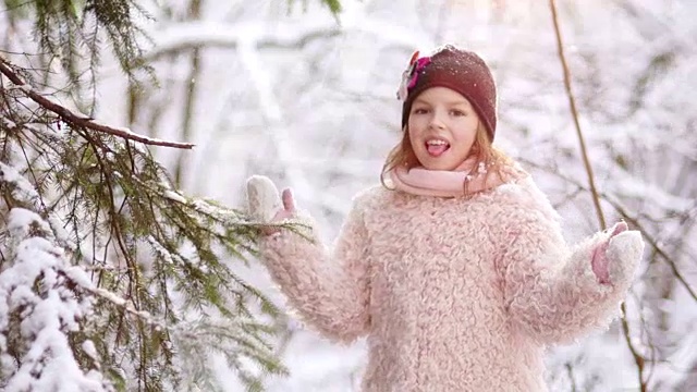 女孩接住了雪花。冬天的公园，白雪覆盖的树，粉红色的外套，度假的孩子视频下载