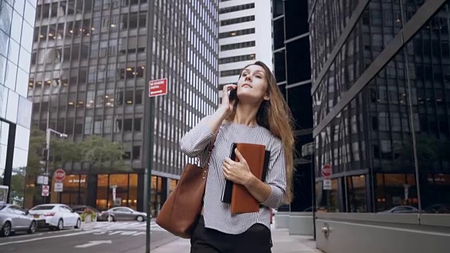 年轻的女商人在美国纽约的金融区边走边打手机。慢动作视频素材