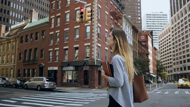 年轻美丽的女商人拿着文件，在纽约金融区过马路。慢动作视频素材