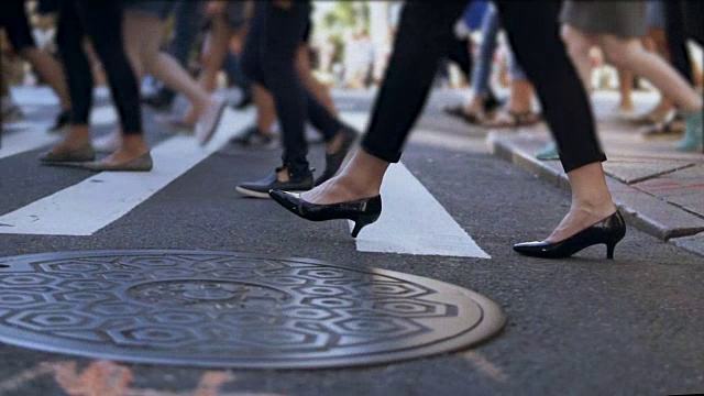 近景时尚女性的脚。女商人正在拥挤的市中心过马路。慢动作视频素材