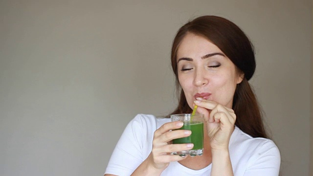 蔬菜排毒净化奶昔-女人通过吸管饮用。女孩微笑着喝着绿色果汁。饮食、健身、健康生活的理念。特写镜头。光背景视频素材