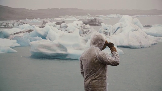 在冰岛，年轻男子站在冰泻湖的雨衣背影。游客独自探索著名景点视频素材