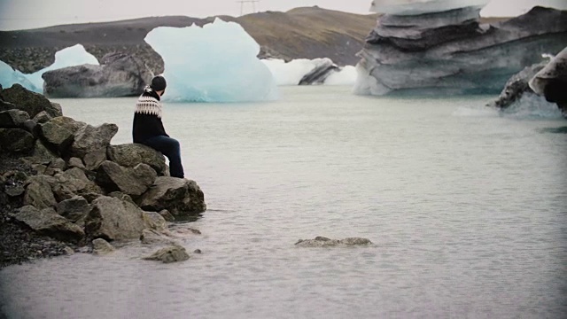 年轻英俊的男子坐在冰礁湖的岩石上欣赏风景。独自探索冰岛的男性视频素材