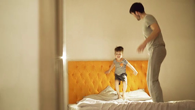 快乐的父亲和小儿子在晚上睡觉前在家里的床上跳舞和玩耍视频素材