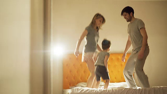 幸福的家庭和小儿子在晚上睡觉前在家里的床上跳舞视频素材