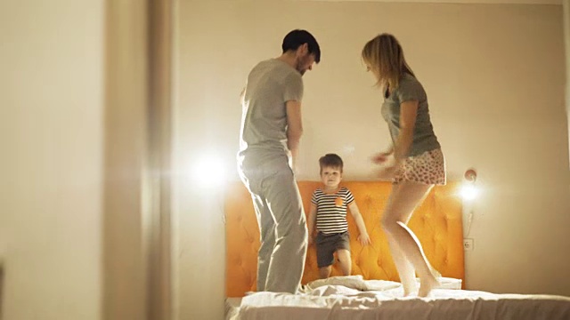 快乐的家庭和小儿子跳舞，在晚上睡觉前在家里的床上玩视频素材