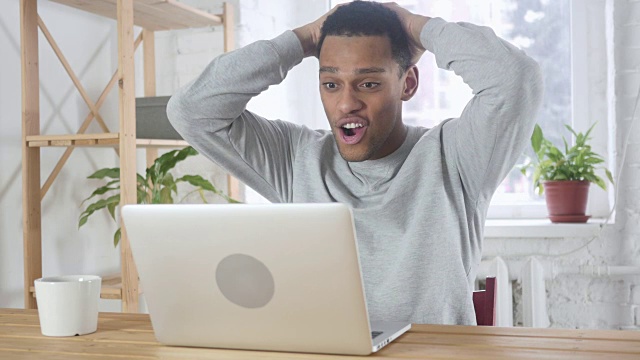 坐在沙发上用笔记本电脑工作的兴奋的美国黑人庆祝成功视频素材