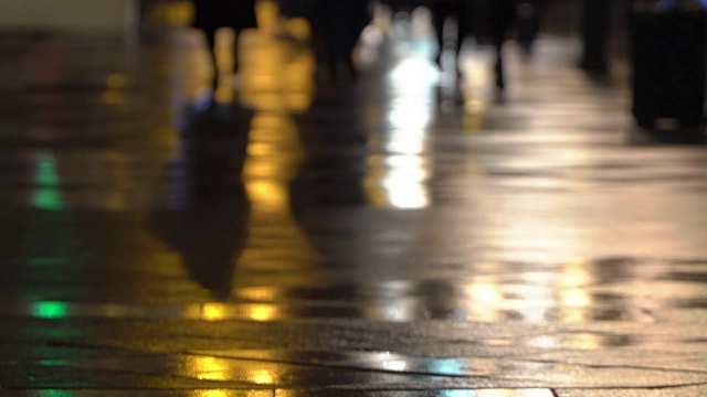 在潮湿的人行道上，街灯映出了辨认不出的人的剪影。长长的影子。雨夜的城市街道上有路灯，沥青路从雨中闪闪发光。不认识的行人，年轻人。夜晚的城市下雨。购物的概念视频素材